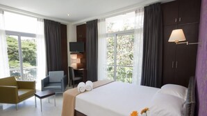 Habitación de hotel moderna con una cama grande, un sofá, un televisor y vistas a zonas verdes.