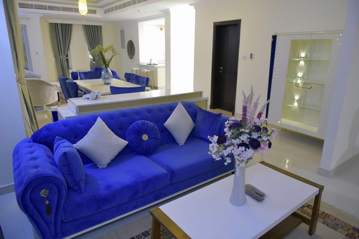 A modern living room with a blue sofa, a white coffee table, and a vase with flowers.
