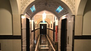 A long, well-lit hallway with a central staircase, ornate ceiling, and patterned walls.