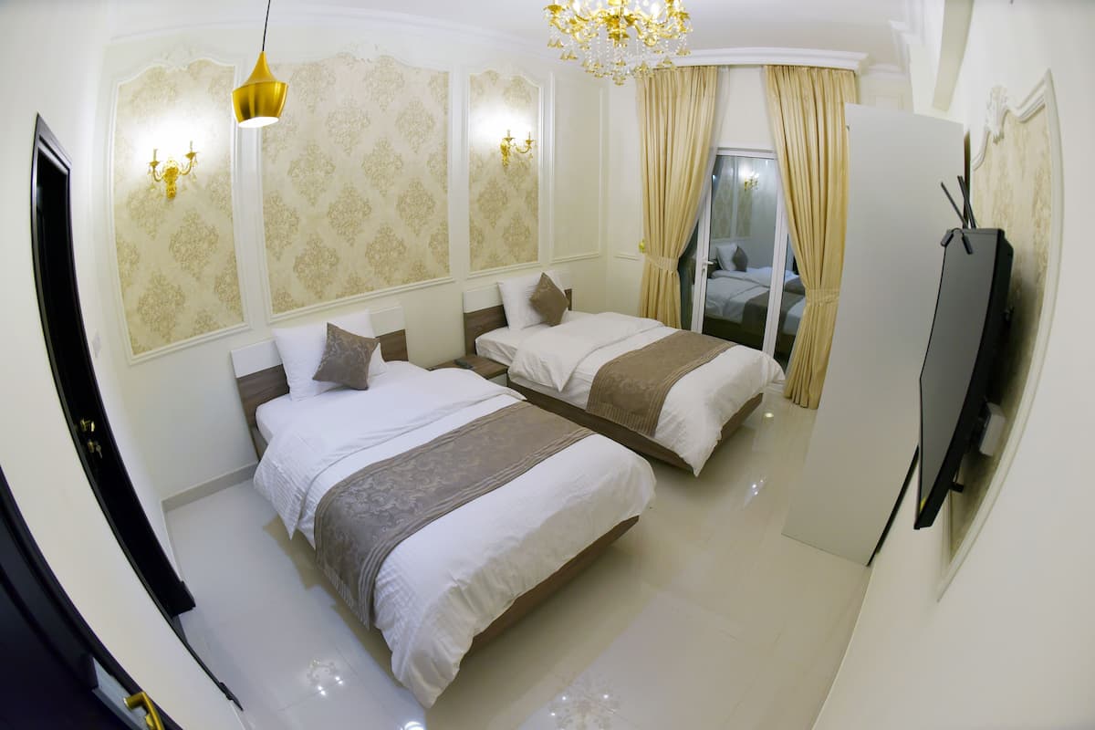 A hotel room with two beds, a chandelier, a television, and a sliding door leading to a balcony.