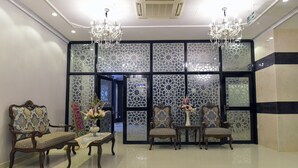 A lobby with ornate chairs, a bench, and a chandelier.