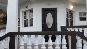 Un edificio blanco con puerta negra, barandillas blancas y un ventanal en el piso superior.