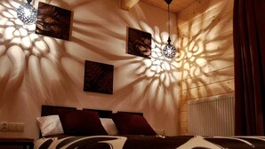 A bedroom with a bed, a nightstand, a wall-mounted radiator, and two wall-mounted lamps casting shadows.
