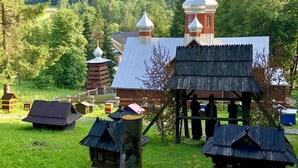 A traditional wooden structure with a bell tower and a thatched roof, surrounded by a lush green landscape.
