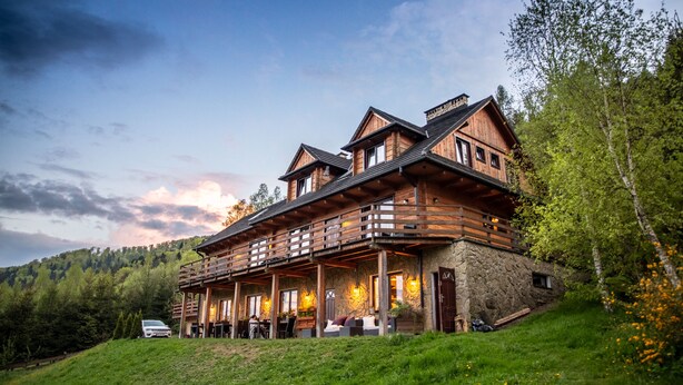 A large wooden cabin with a stone foundation, multiple balconies, and a porch area.