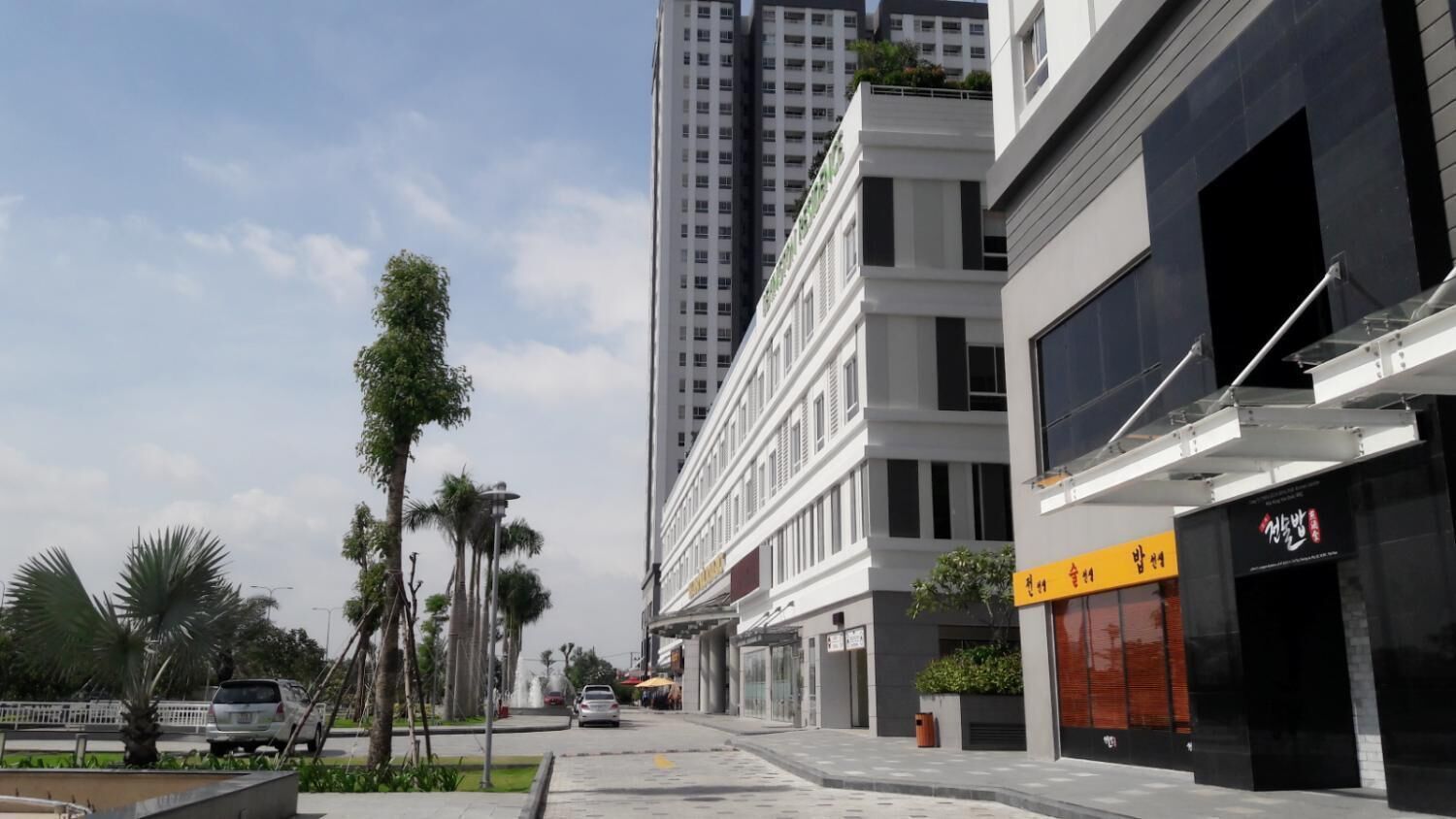 Una calle urbana moderna con edificios altos, palmeras y cielo despejado.