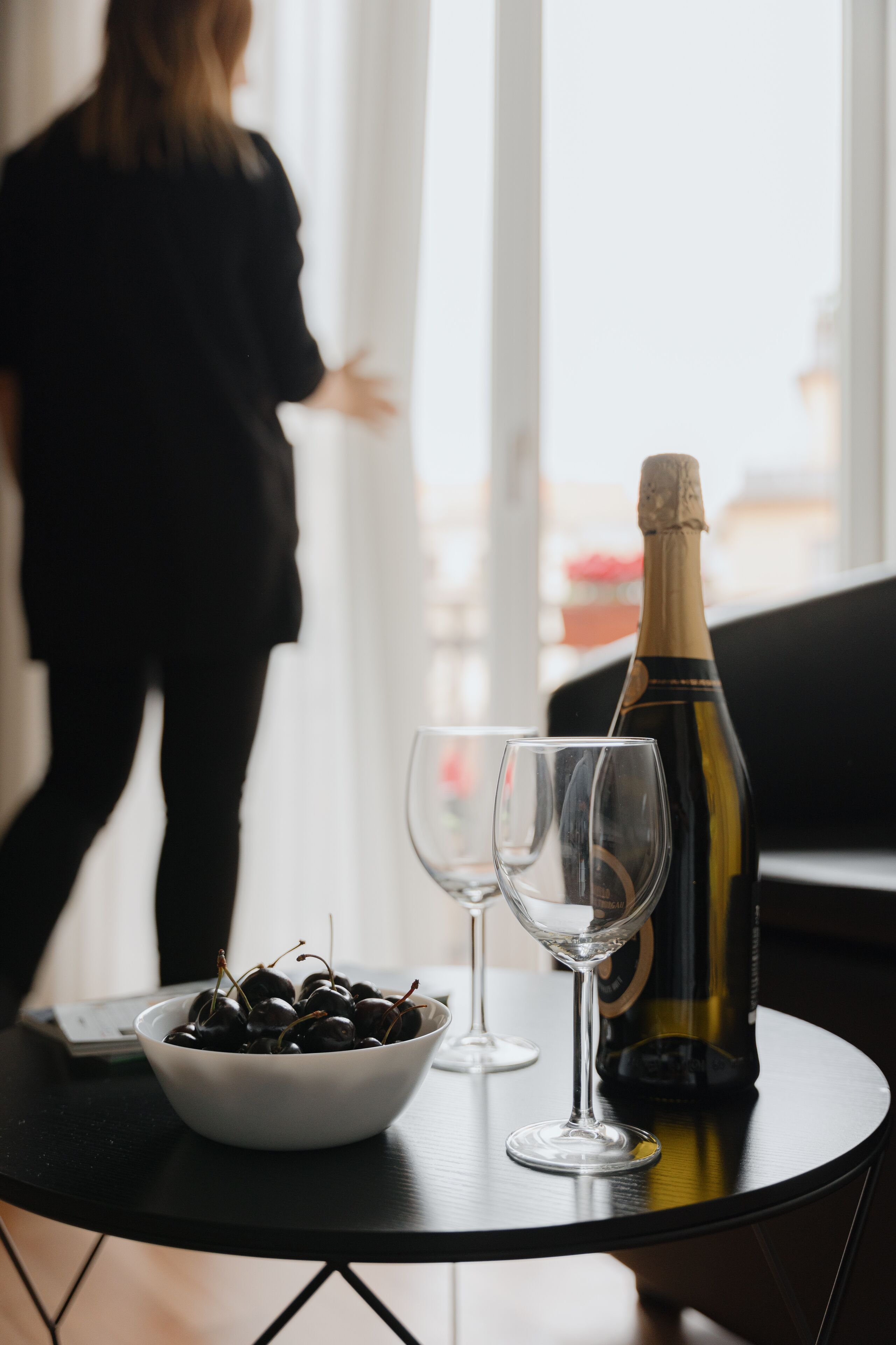A table with a bottle of champagne, two glasses, and a bowl of cherries.