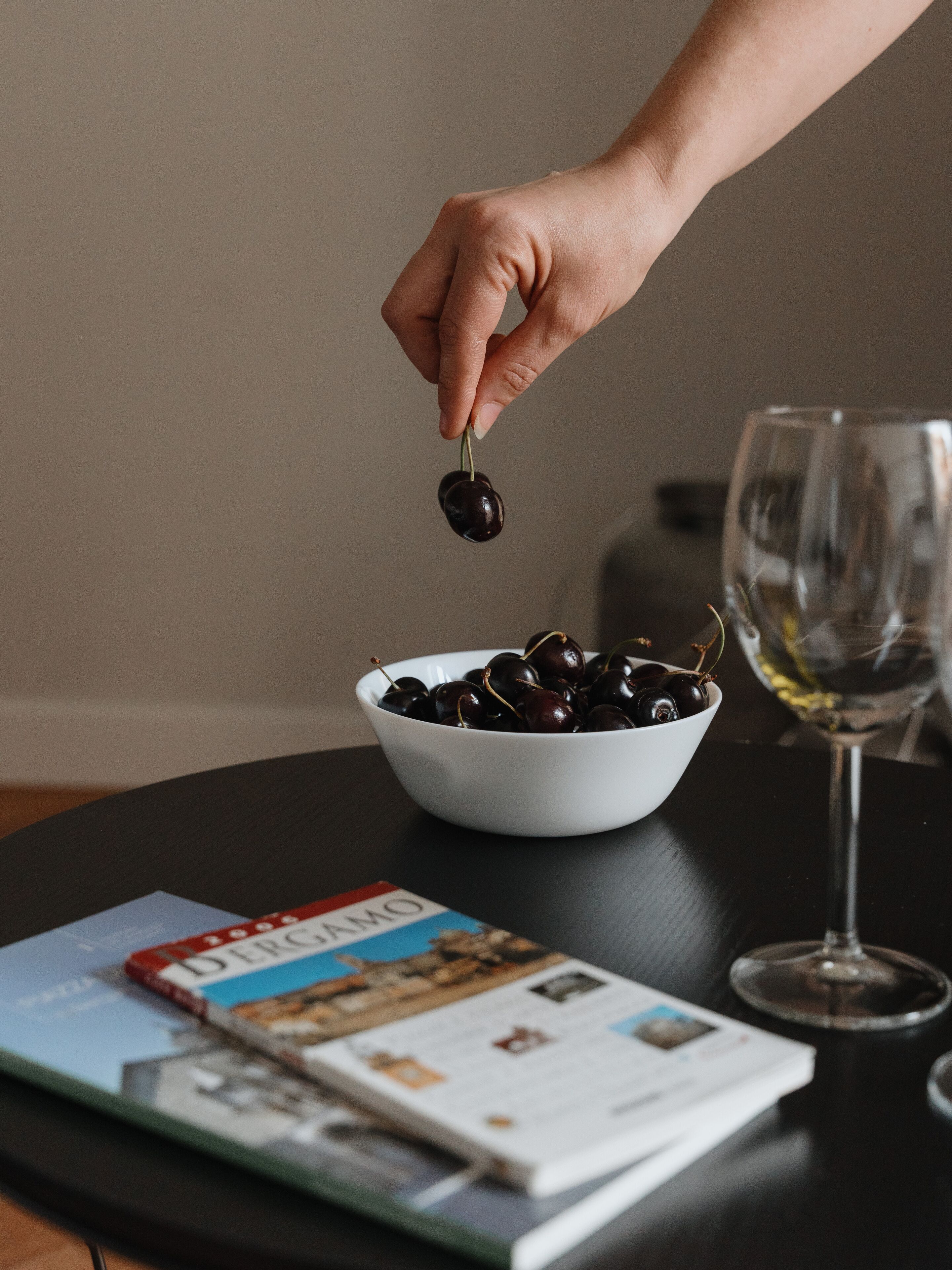A bowl of cherries on a table with a wine glass and a magazine.