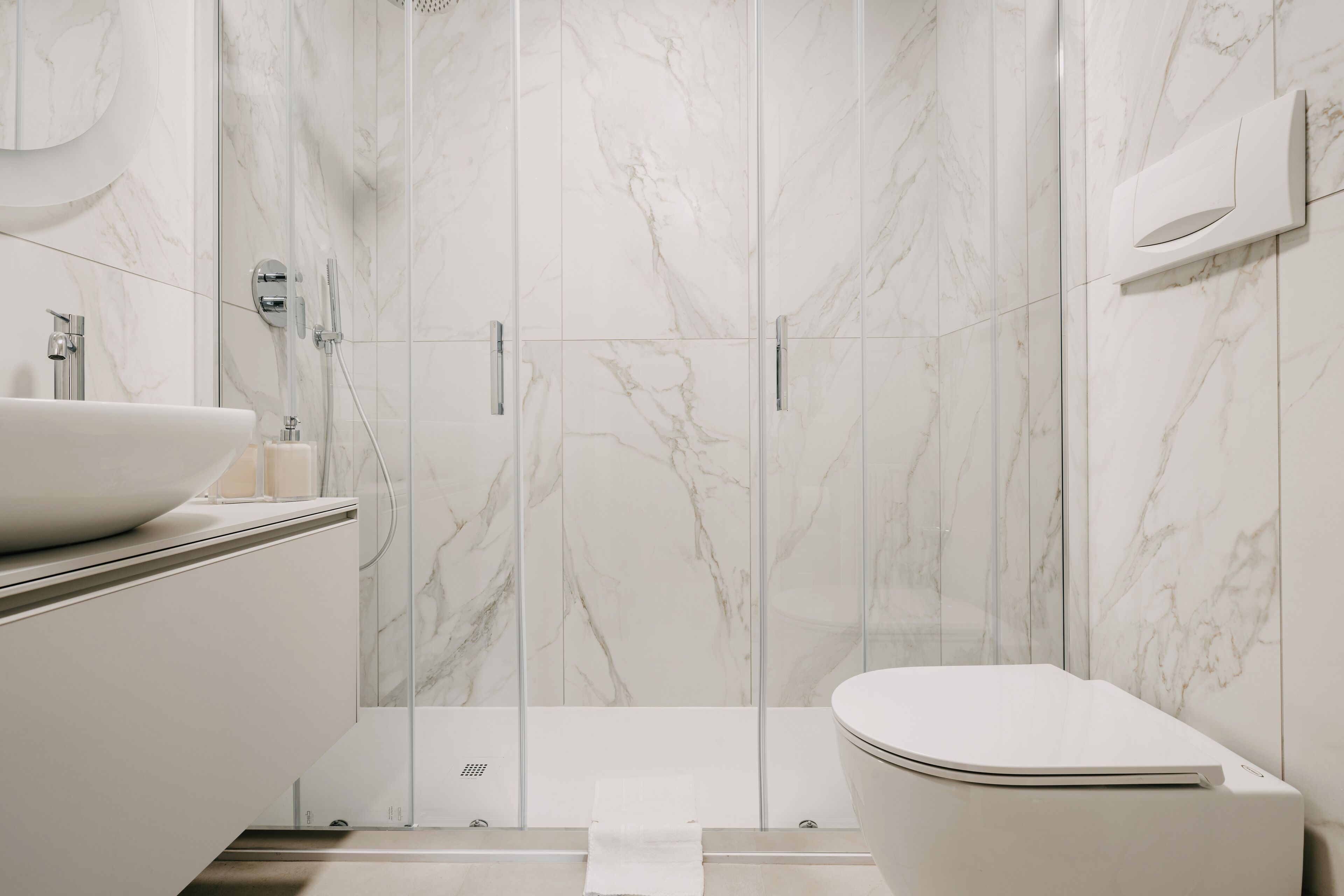 Ein modernes Badezimmer mit einer Duschkabine aus Marmor, einem weißen Waschbecken und einer Toilette.