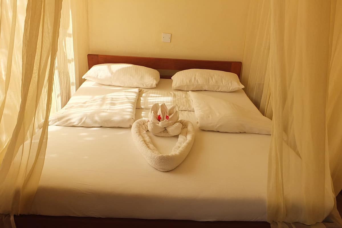 Una cama bien hecha con sábanas y almohadas blancas, un cabecero de madera y una toalla decorativa con forma de cisne sobre la cama.