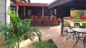Un área de bar al aire libre con piso de baldosas, taburetes y una barra con botellas.