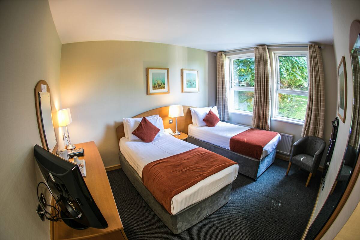 A hotel room with two beds, a desk with a computer, a chair, and a window with curtains.