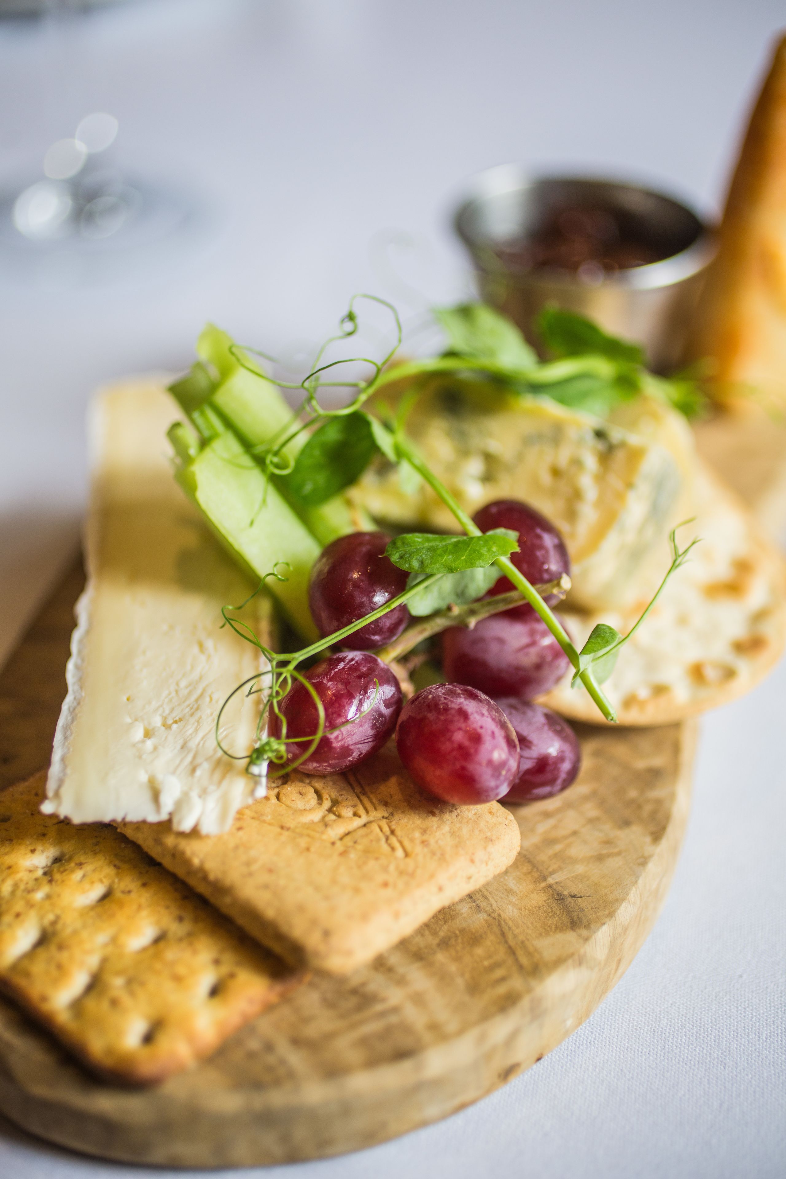 A wooden board with a variety of cheeses, grapes, and crackers.