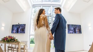 A couple in wedding attire standing in a bright room with large windows and artwork on the walls. - Rosspark Hotel (Ballymena)