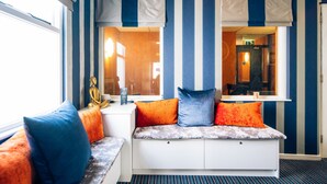 A room with a striped blue and white wall, a window with curtains, a bench with cushions, and a statue on the windowsill. - Rosspark Hotel (Ballymena)