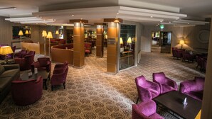 A hotel lobby with patterned carpet, purple seating, and a reception area with a glass partition. - Rosspark Hotel (Ballymena)