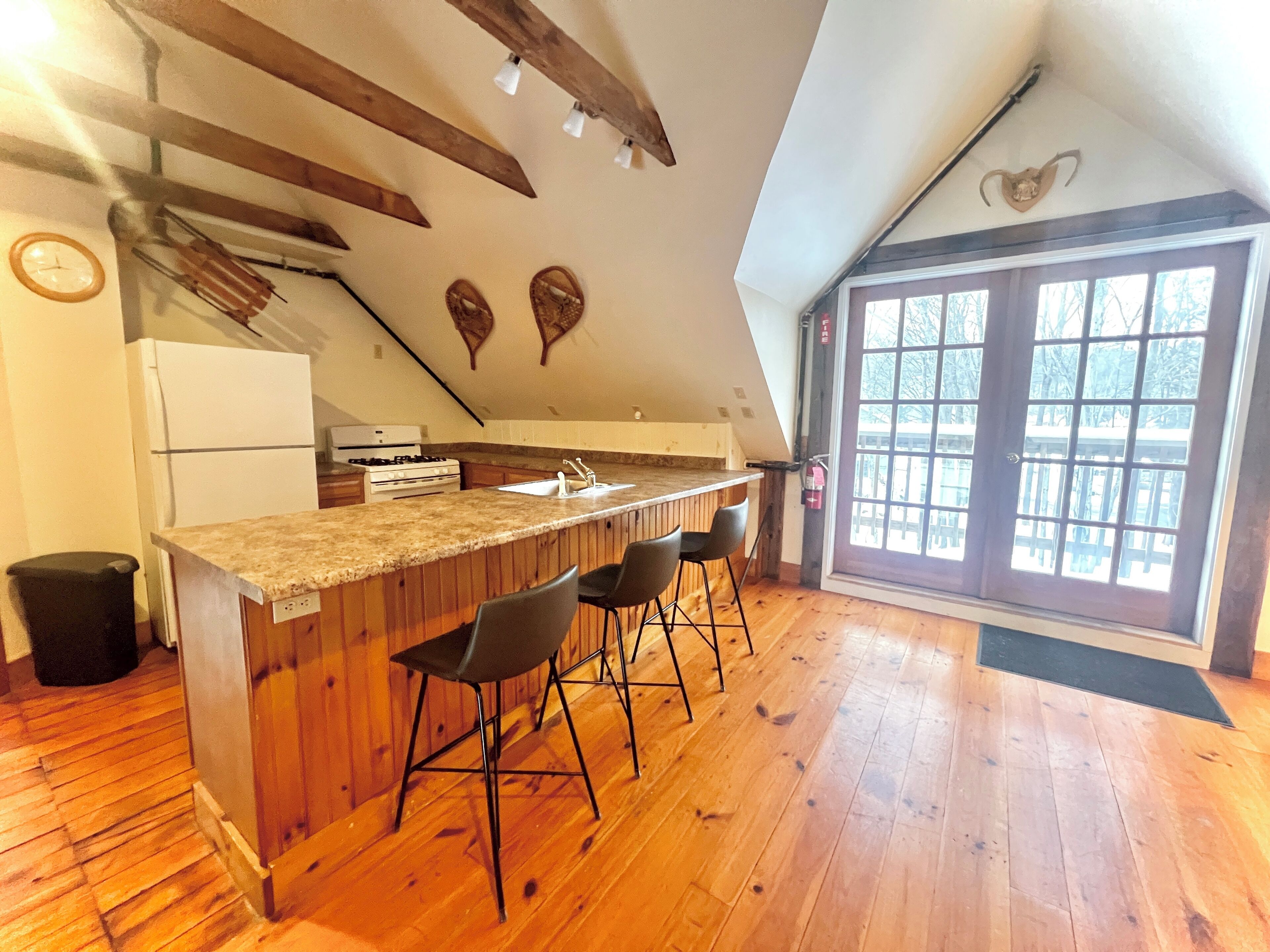 Una cocina con vigas de madera, una barra con taburetes, un refrigerador y un ventanal con vistas.