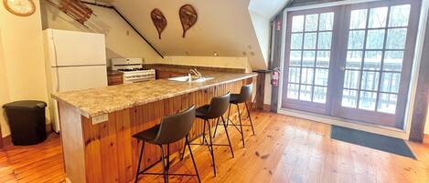 Una cocina con vigas de madera, una barra con taburetes, un refrigerador y un ventanal con vistas.