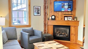 Una sala de estar acogedora con chimenea, sofás grises, una mesita de centro y un televisor de pantalla plana sobre la chimenea.