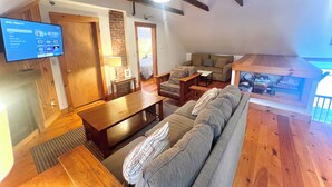 Un salón acogedor con techo de madera, televisor montado en la pared, sofá, mesa de centro y estantería.