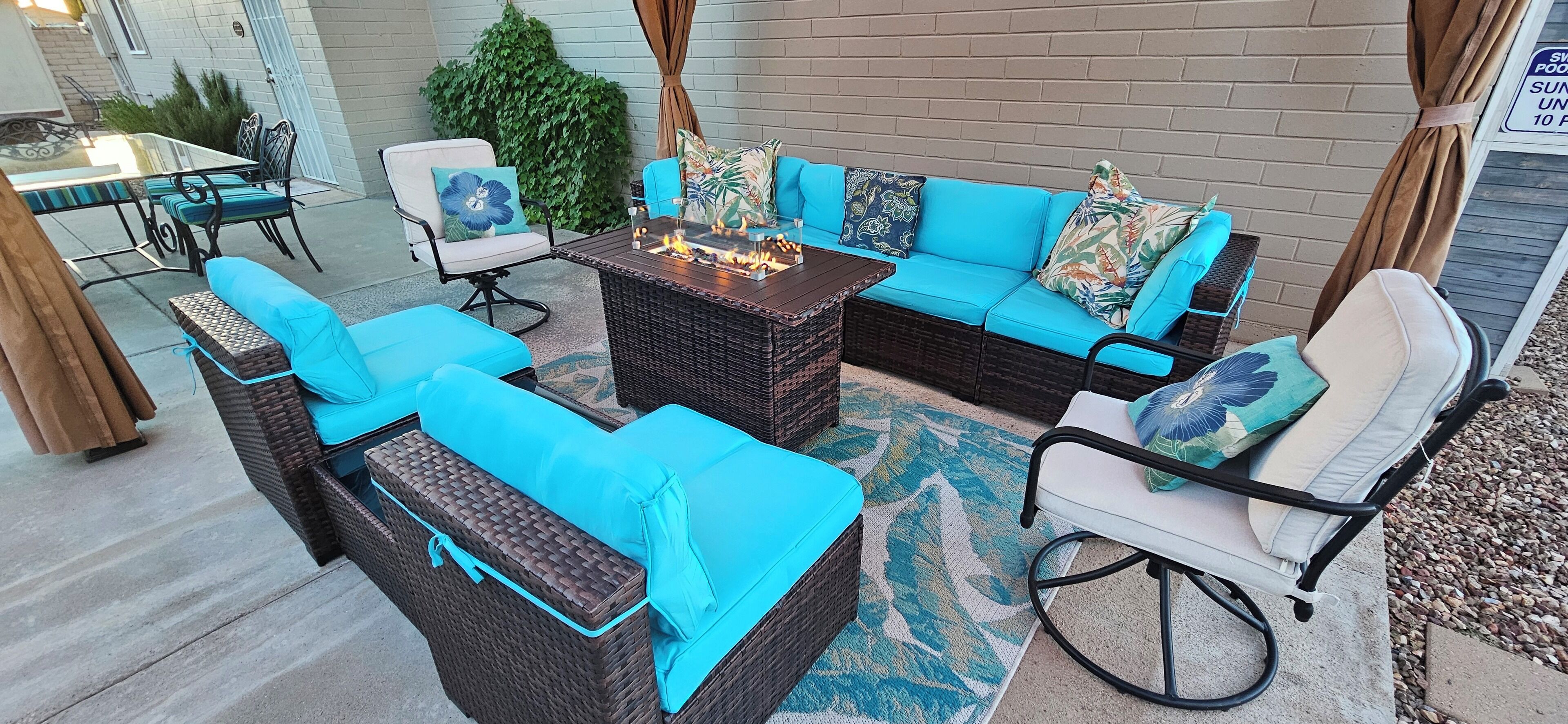 A patio area with wicker furniture, a fire pit, and a glass table.