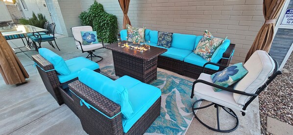 A patio area with wicker furniture, a fire pit, and a glass table.
