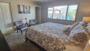 A bedroom with a large bed, two chairs, a small table with a vase, and a window with a view of the outside.