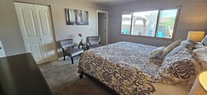 A bedroom with a large bed, two chairs, a small table with a vase, and a window with a view of the outside.