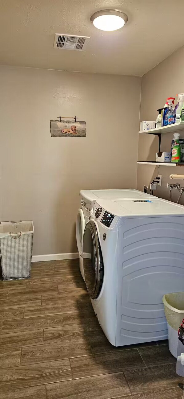 Un lavadero con lavadora, tendedero y estante con productos de limpieza.