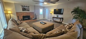 Una sala de estar con un sofá modular, una chimenea, un televisor y un ventilador de techo.