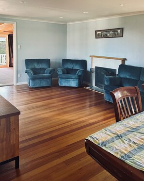 A room with a wooden floor, two blue armchairs, a wooden coffee table, and a framed picture on the wall. - Pirate Adventure Meets Lake Taupō Living | Spacious Family & Group Accommodation (Taupo Central)