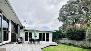 Une maison avec une terrasse, un patio avec des chaises et une pelouse.