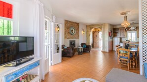 A spacious living room with a television, seating area, and a kitchen in the background. - Moorish-Style Mountain Villa: Stunning 360° Views, Pool & Hot Tub (Torrox)