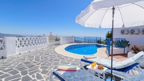 A rooftop pool area with a clear view of the sea, lounge chairs, and a white umbrella. - Moorish-Style Mountain Villa: Stunning 360° Views, Pool & Hot Tub (Torrox)