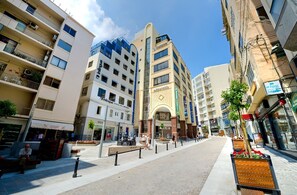 A modern urban street with multi-story buildings, a central plaza with benches, and a clear sky. - SEAFRONT LUXURY APARTMENT incl POOL (Sliema)