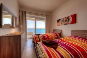 A hotel room with two beds, a wooden dresser, a large window with curtains, and a painting on the wall. - SEAFRONT LUXURY APARTMENT incl POOL (Sliema)