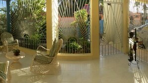 A sunlit outdoor patio with wicker furniture and a car parked behind a metal gate. - Nicole's Guest Home (Higuey)