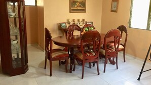 A dining room with a round wooden table surrounded by six chairs, a glass cabinet, and a painting on the wall. - Nicole's Guest Home (Higuey)