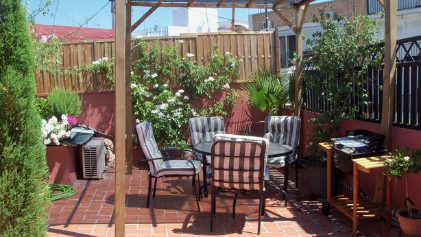 A patio with a wooden pergola, striped chairs, a small table, and potted plants. - ATTIC + PRIVATE TERRACE AND FREE WIFI (Sevilla)