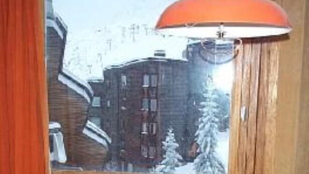 A room with a large window, a table with a colorful tablecloth, and a chair. - Residential flat (Morzine)