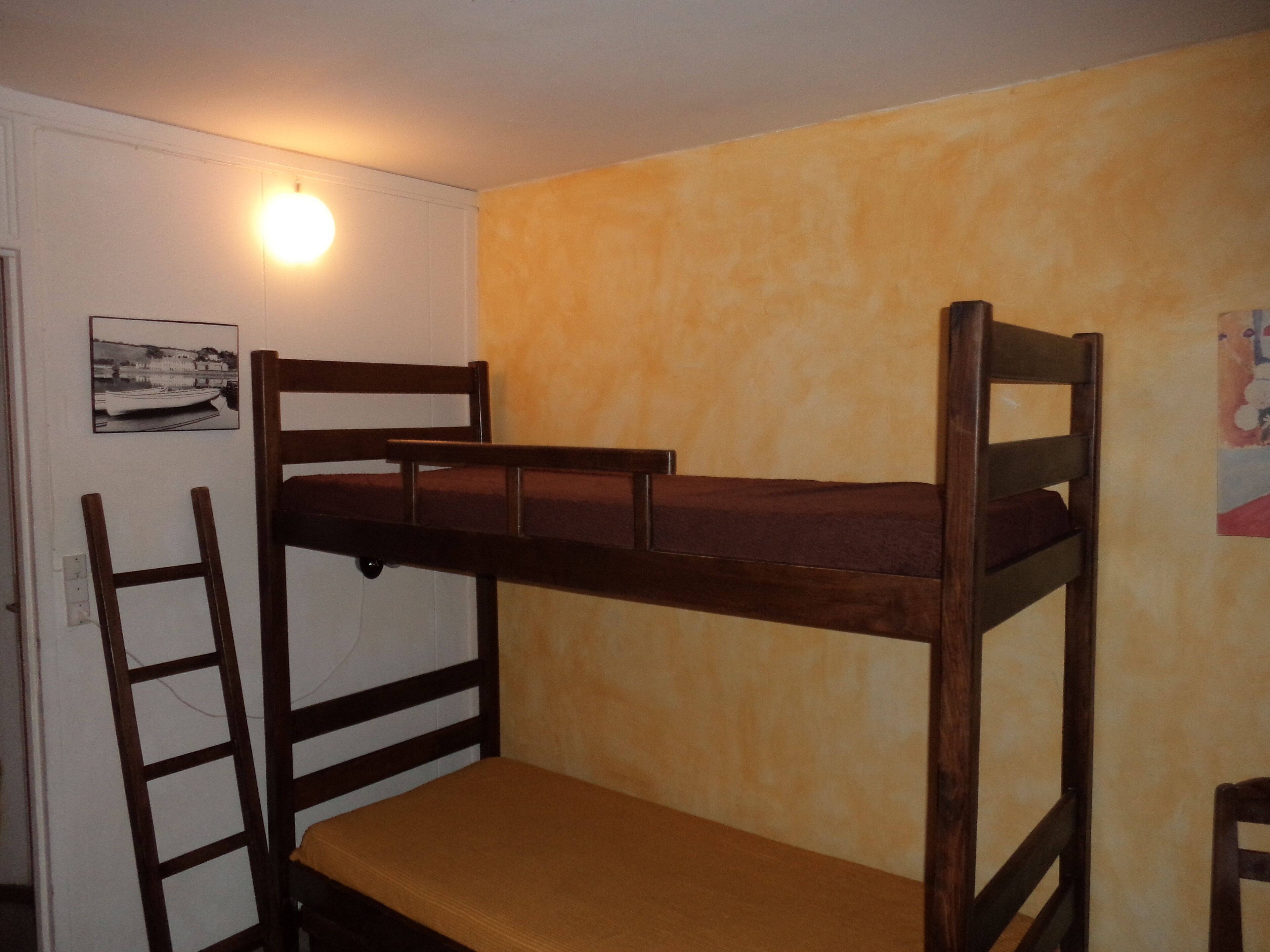 Ein Stockbett mit einer Leiter, ein einzelner Stuhl und eine Wandleuchte.