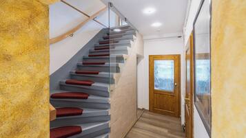 Eine moderne Treppe mit Glastrennfeldern und roten Stufen, die zu einer Holztür mit satinierten Glasscheiben führt.