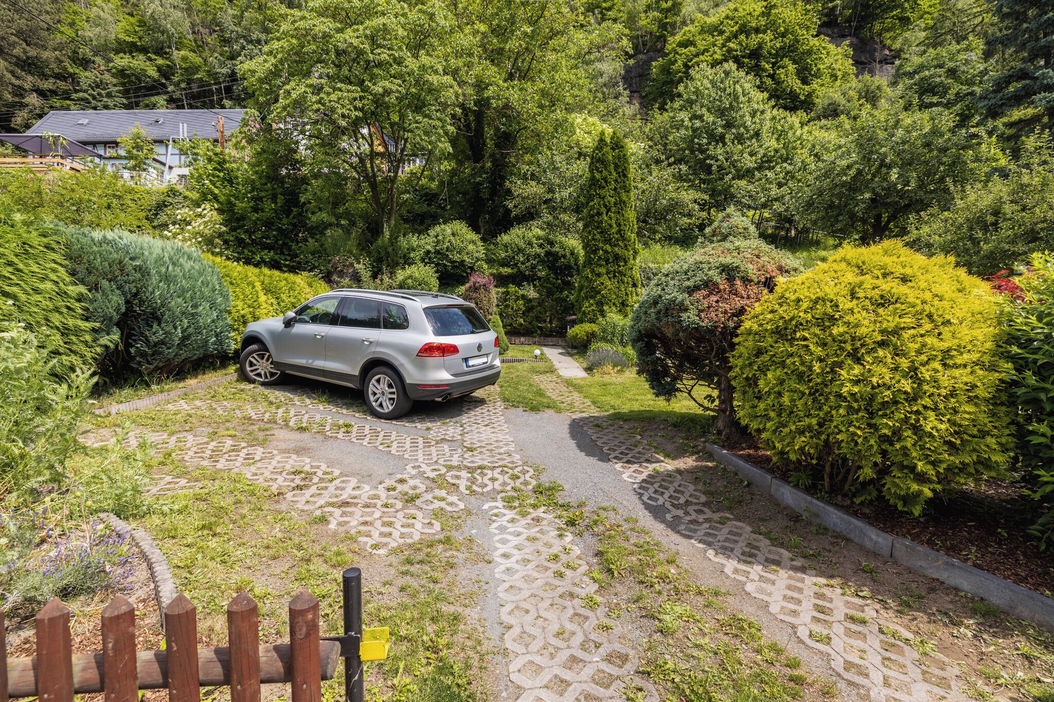 A car parked on a paved path surrounded by lush greenery and a wooden fence.
