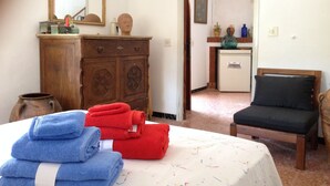 Een kamer met een bed, een houten dressoir, een stoel en een kleine keukenhoek.