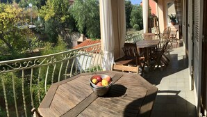 A wooden table with a metal bowl of fruit on a balcony with a railing, overlooking a garden and buildings. - Nice apartment in a character villa next to the sea in Banyuls (Banyuls-Sur-Mer)