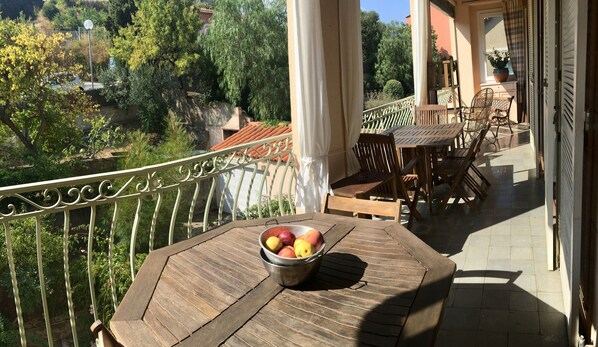 A wooden table with a metal bowl of fruit on a balcony with a railing, overlooking a garden and buildings. - Nice apartment in a character villa next to the sea in Banyuls (Banyuls-Sur-Mer)