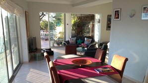 Un coin repas avec une table dressée pour quatre personnes, entourée de chaises, dans une pièce dotée d’une grande porte-fenêtre coulissante donnant sur un patio extérieur.