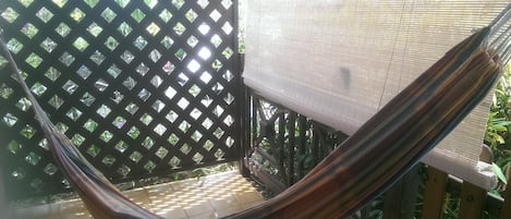 Un fauteuil suspendu dans un espace extérieur ombragé, agrémenté d’une clôture en treillis et d’un banc à l’ombre.