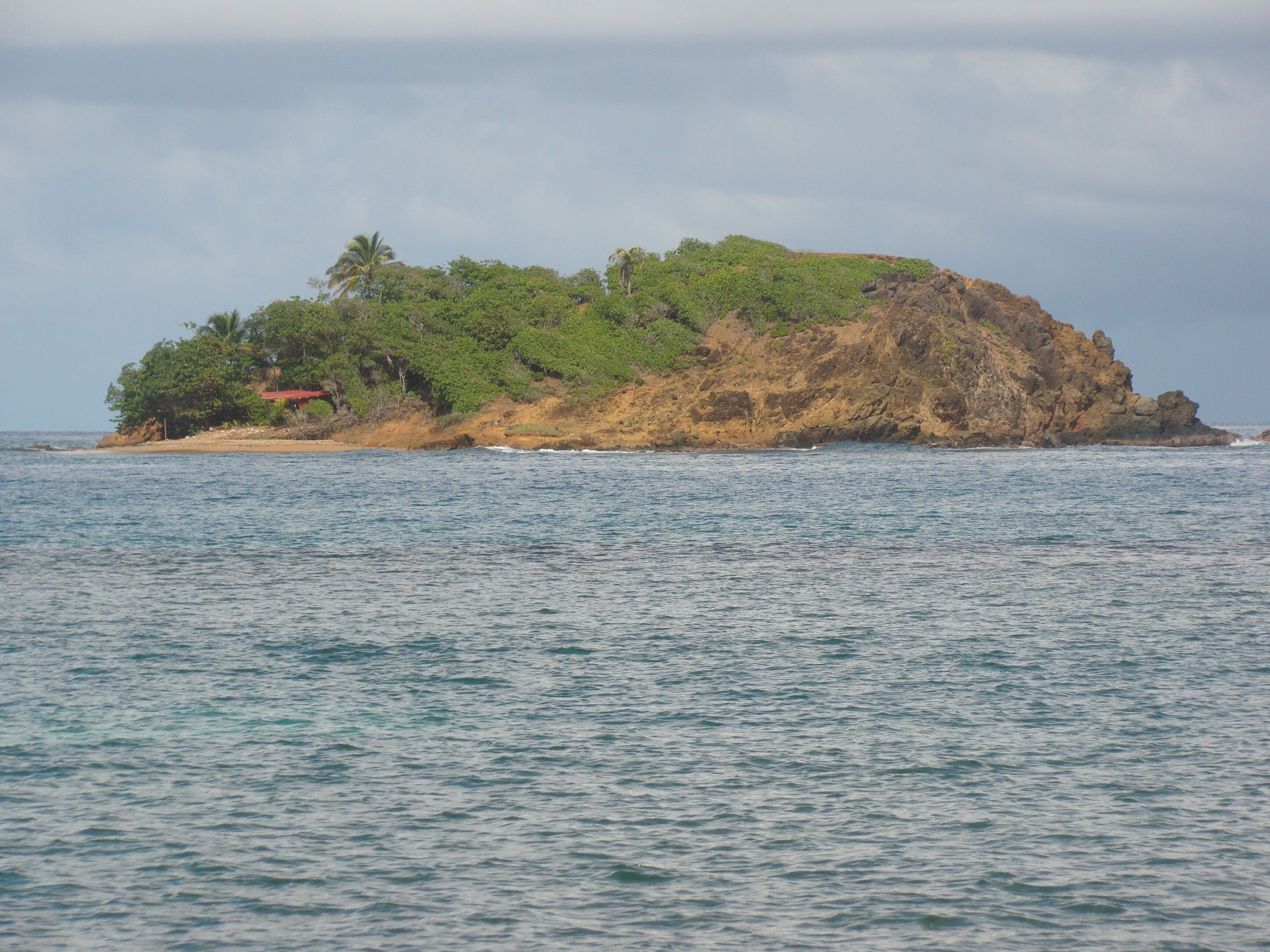 Une petite île couverte d’une végétation luxuriante et abritant quelques bâtiments, entourée d’une mer calme.