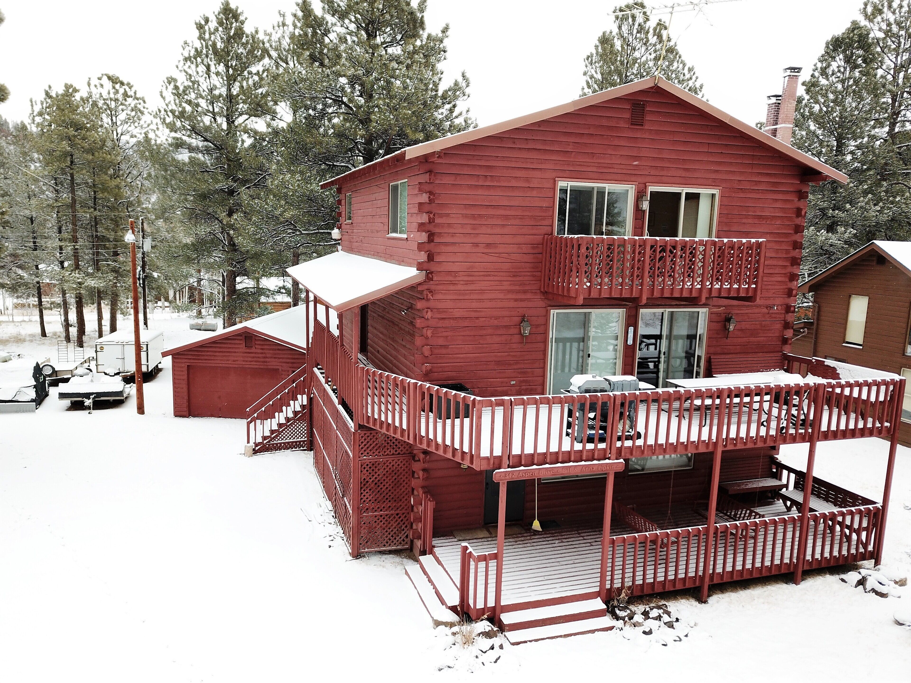 Une cabane en rondins à deux étages, dotée d’un balcon et d’une véranda couverte.